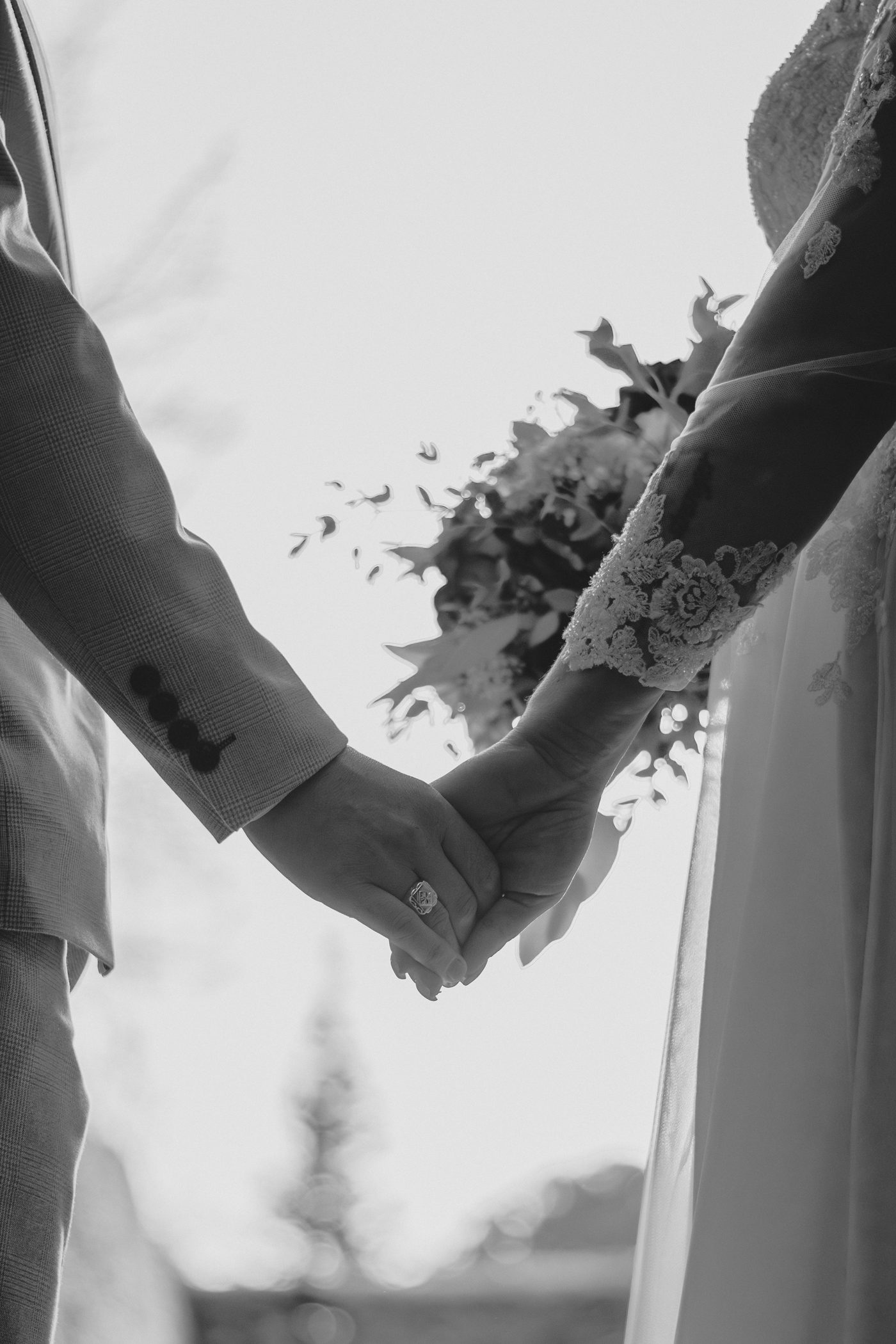 Black and white photograph of a bride and groom holding hands with her bouquet