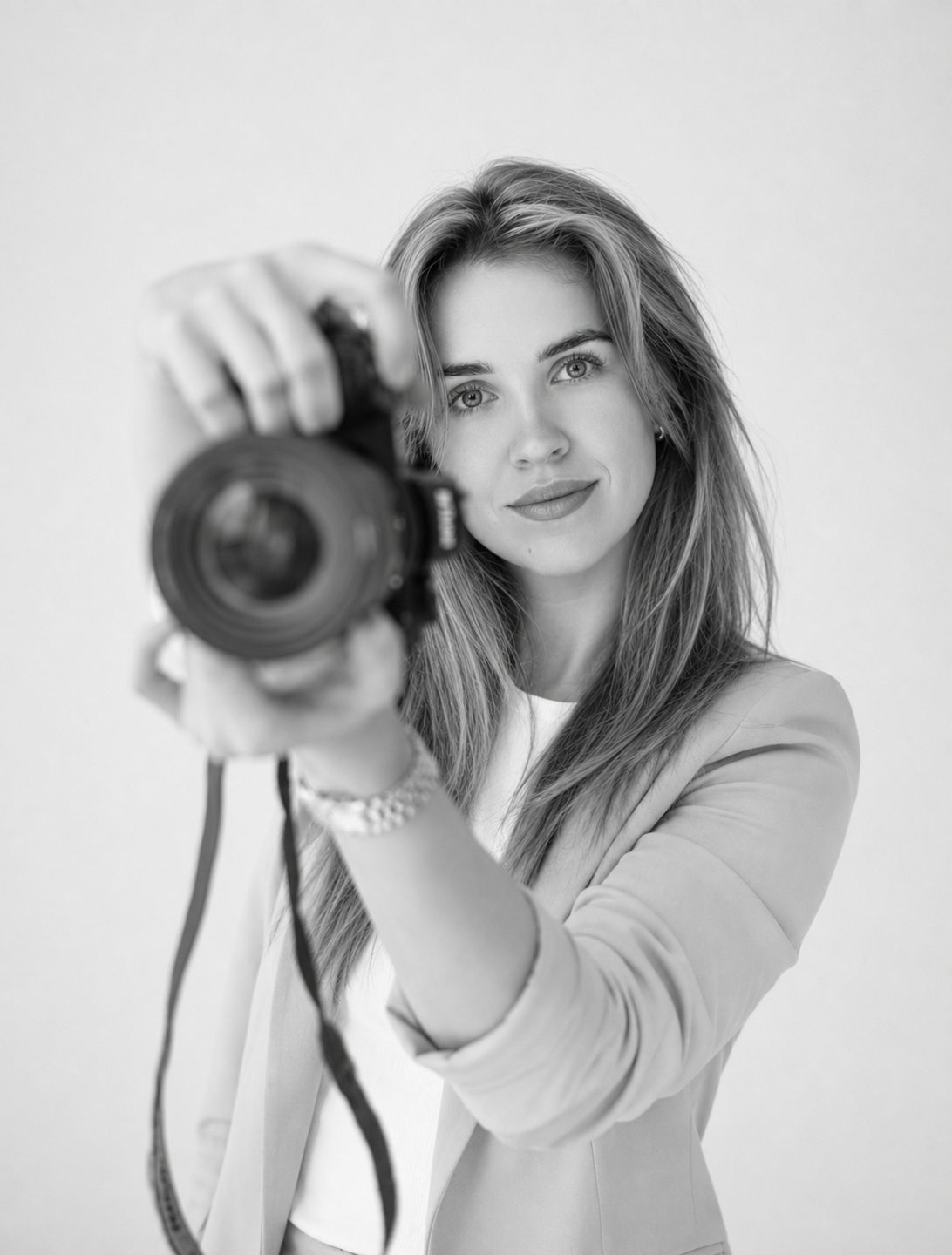 Black and white portrait of Emilija holding her camera up towards the viewer