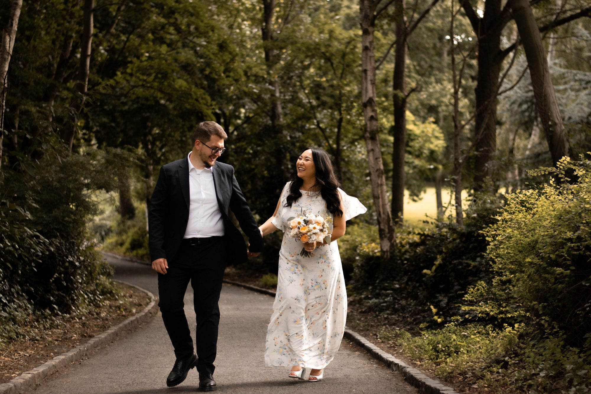 Newlyweds walking hand in hand along a woodland path in soft evening light